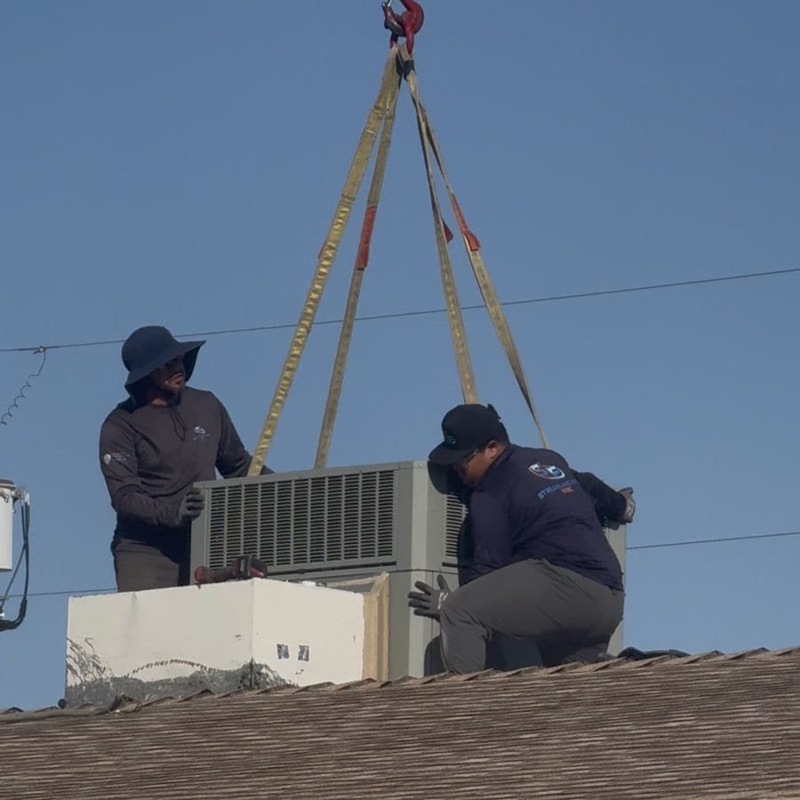 Technicians guiding a rooftop package unit during crane placement